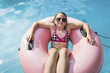 © Cavan Images - High angle view of girl wearing sunglasses resting on inflatable ring in swimming pool