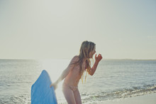 Cheerful Girl Holding Surfboard On Beach Against Sky