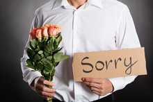 Man Holding Roses And Text Sorry Written On Cardboard