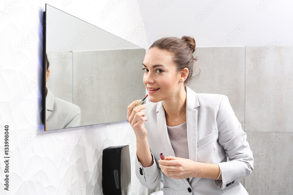 Kobieta maluje usta w biurze. Atrakcyjna kobieta biznesu maluje usta pomadką w firmowej łazience - obrazy, fototapety, plakaty 