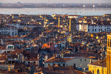 Wall Mural - Aerial view of Venice, Italy, at sunset with rooftops of building, the sea and warm sunlight.