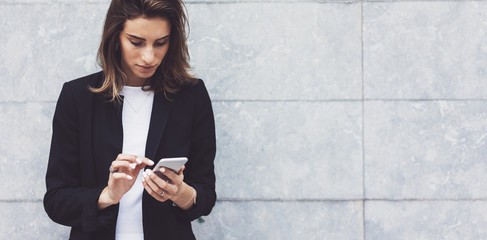 Portrait young businesswomen in black suit using smartphone isolated on background concrete gray wall mockup, pretty hipster manager holding mobile gadget, girl smiletexting message, connect