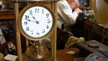 Vintage Torsion Pendulum Clock On Table While Horologist Working In Background