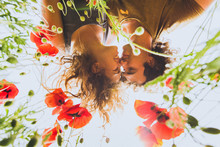 Young Happy Couple With Curly Hair Enjoying In Bright Red And Yellow Blossoming Field