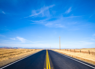 Asphalt road through a golden yellow grass field and clouds in blue sky in summer day