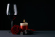 Wineglass with rose, candle and chocolate candies on dark background. Love card concept with copy space. Valentine's day theme