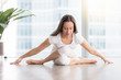 © fizkes - Young attractive woman practicing yoga in apartment, sitting in variation of Gomukasana exercise with forward bend, Cow Face pose, working out, wearing white sportswear, indoor full length