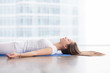 © fizkes - Closeup side view of young attractive woman practicing yoga, lying in Savasana exercise, Dead Body, Corpse pose, working out, wearing sportswear, white t-shirt, indoor, floor window with city view