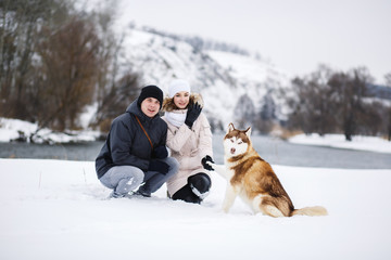 A young pregnant couple walking in the woods with the dog red Husky.