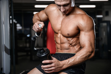 Wall Mural - Handsome fitness model holding a shaker in the gym gain muscle.