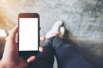 Mockup image of hand holding black mobile phone with blank white screen  with white canvas shoes on concrete polishing wall