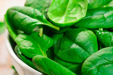 Fresh spinach leaves in a white bowl on the old wooden backgroun