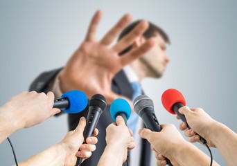 Many reporters are recording with microphones a politician who shows no comment gesture.