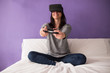 © Manuel - Young woman sitting on the bed at home having fun playing a virt