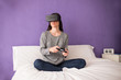 © Manuel - Young woman sitting on the bed at home having fun playing a virt