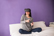 © Manuel - Young woman sitting on the bed at home having fun playing a virt