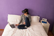 © Manuel - Young woman sitting on the bed at home relaxing and using virtua