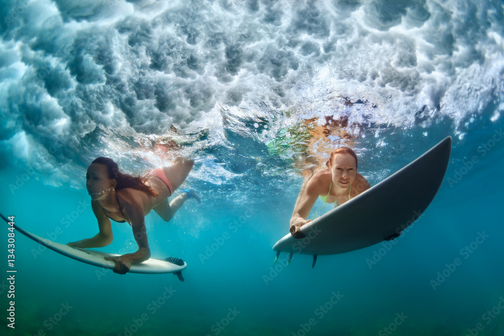 Group of active girls in action. Surfer women with surf board dive underwater under breaking big wave. Healthy lifestyle. Water sport, extreme surfing in adventure camp on family summer beach vacation - obrazy, fototapety, plakaty 