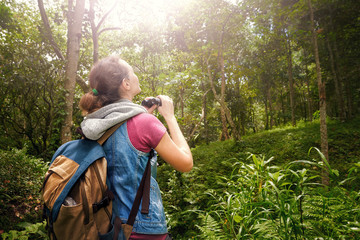 traveller with backpacker watching through binoculars wildlife birds in the jungle.