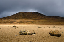 Desolate Moonscape In The National Park Of Mount Kilimanjaro. Rocks Lay A Moon Like Landscape Extending To A Hill That Is Surrounded By Dark Clouds. 