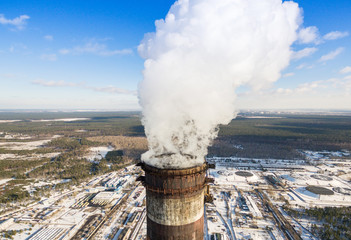 Heat electric station in winter. Aerial view. From above. Power station in a forest in sunny weather. Pipe with smoke close up