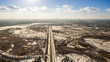 © LALSSTOCK - Panorama of forest with highway in the middle on a background of urban development in winter on a sunny day. Aerial view.