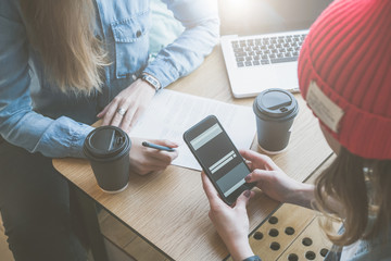 Wall Mural - Top view, close-up smartphone in female hands. Meeting of two friends in cafe.Girls learn online, drinking coffee. First woman takes notes,and second uses a smartphone.Freelancers work outside office.