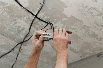 Electricians cleans the contacts with pliers. Installing the ceiling light.