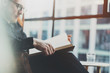 Closeup portrait of pensive bearded businessman reading book while sitting in vintage chair.Young man relaxing at home.Selective focus on hands,blurred background.Horizontal, film effect.