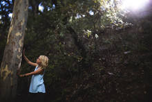 Girl Touching Tree Trunk In Forest