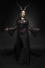 Young Woman In Black Fantasy Costume With Big Horns On Dark Background