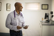 © Erickson Stock - Smiling mid adult doctor holding a digital tablet while standing indoors