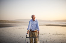 Portrait Of A Senior Man Standing On A Beach With A Walking Aid.