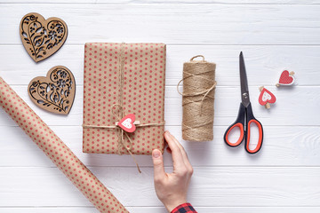 Wall Mural - Flat lay composition packaging of gifts on Valentine's Day, a birthday or Mother's Day with women hand gifts, scissors, wrapping paper and twine. White wooden background. Top view.