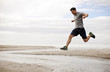 © Erickson Stock - Young man jumping over shallow water on a beach.
