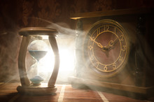 Time Concept. Silhouette Of Hourglass Clock And Old Vintage Wood Clock With Arrow And Smoke On Dark Background With Hot Yellow Orange Red Blue Cold Back Lighting, Or Symbols Of Time With Copy Space