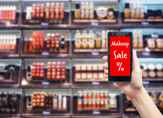 Makeup and beauty sale concept. Female hand with smartphone on blurred showcase background