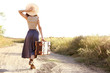© Africa Studio - Young woman with suitcase walking along countryside road