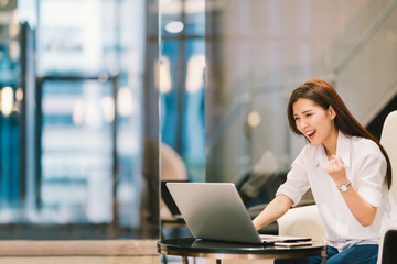 Beautiful Asian girl celebrate with laptop, success happy pose. E-commerce, university education, internet technology, or startup small business concept. Modern office or living room with copy space