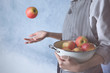 Woman in apron holding colander with juicy apples on blue background, closeup
