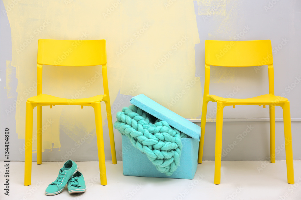 Yellow chairs and blue box with knitted plaid on colour wall background