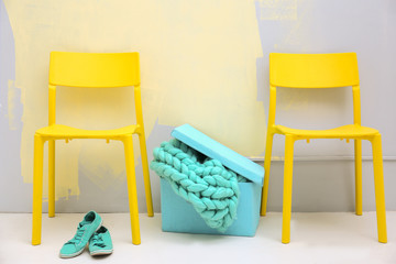 Yellow chairs and blue box with knitted plaid on colour wall background