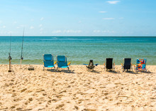 Row Of Empty Beach Chairs And Fishing Poles On The Beach Facing The Ocean