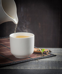 Wall Mural - green tea pouring into tea cup on dark wooden backgroud.