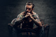 © Fxquadro - Tattooed bearded male sits on a chair.