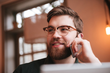 Poster - Happy bearded young man talking by phone and using laptop.