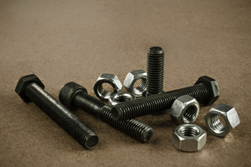 Black bolts and silver nuts scattered on a wooden working table. Picture taken in with soft-box studio.