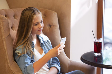 Wall Mural - Pretty teenager girl using mobile phone while sitting in cafe