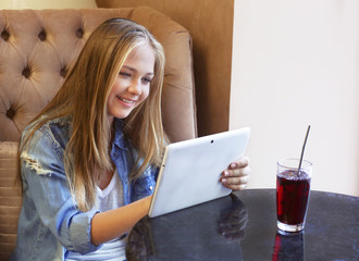 Wall Mural - Pretty teenager girl using tablet computer while sitting in cafe