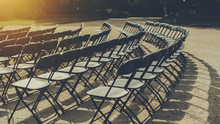 Empty Seat Rows Of Folding Chairs On Ground Before A Concert, Parallel And Rounded Arranged, Multiple Black Chairs On Street On Sunny Day In Park